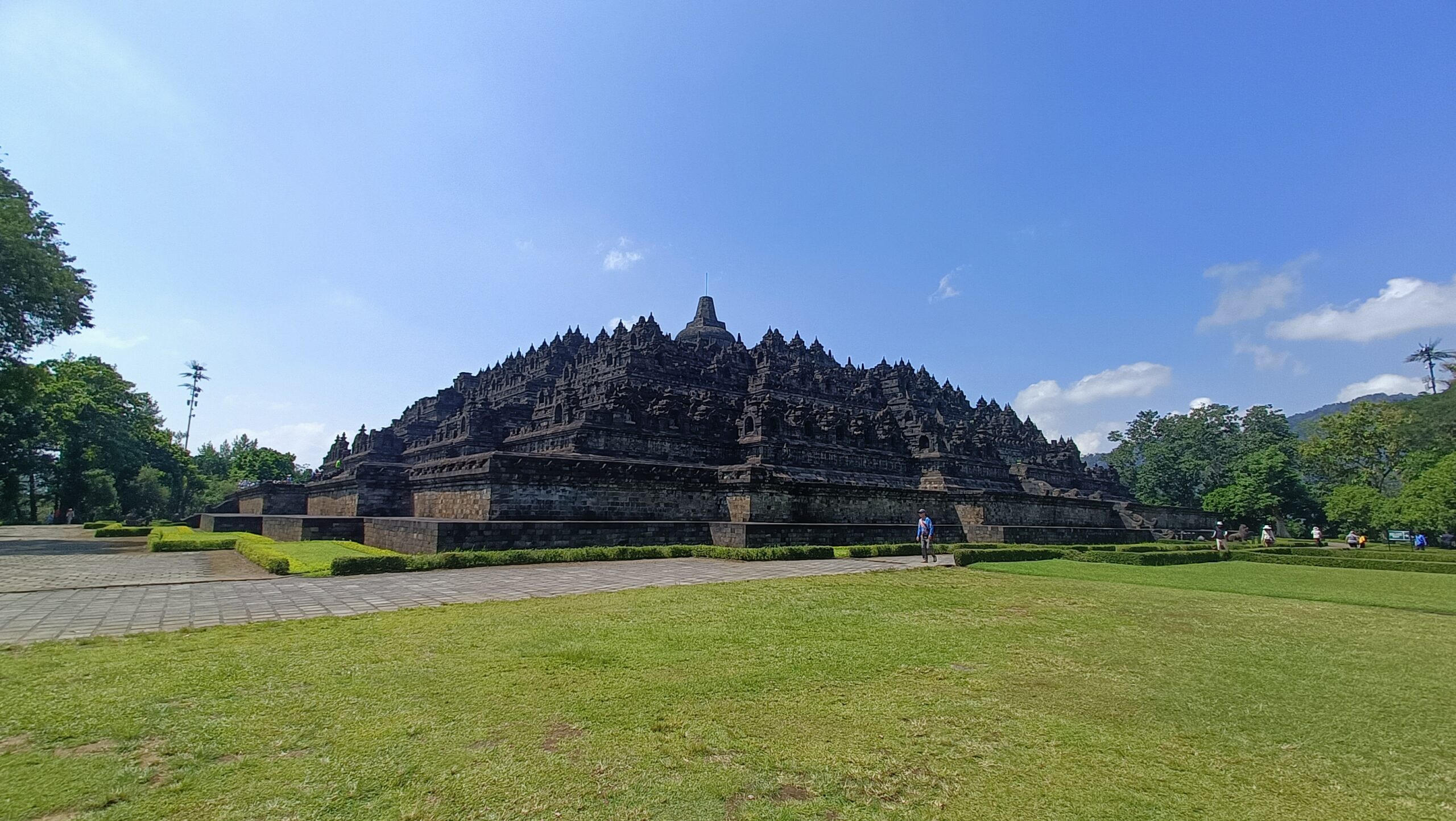 Full view of Borobudur Buddhist temple nine stacked platforms and central dome from grass lawn with blue sky Central Java Indonesia