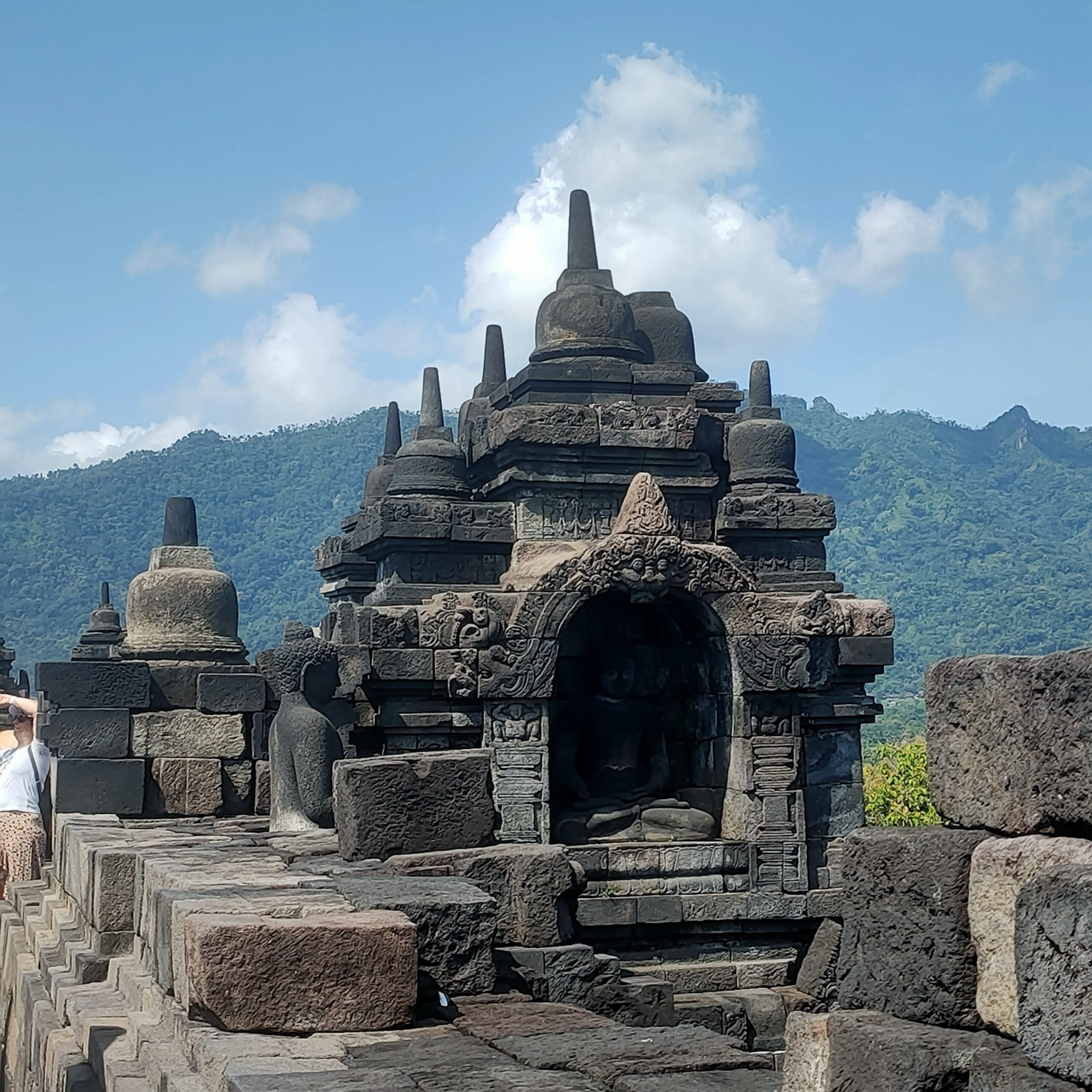 Square stone stupa shrine with arched doorway on Borobudur upper terrace with Mount Merapi volcano background Central Java Indonesia