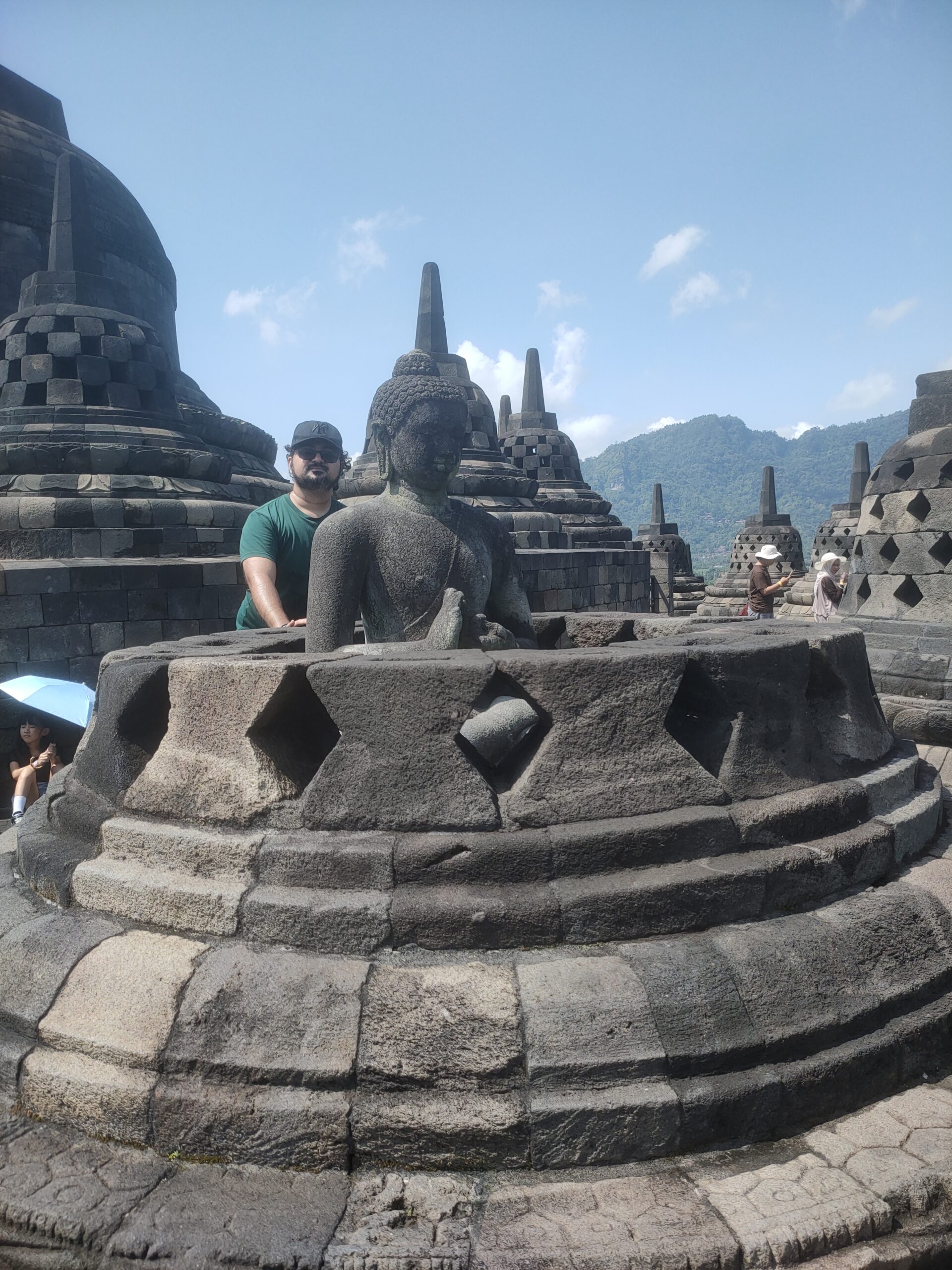 Borobudur Buddha statue inside diamond-patterned stone stupa with tourist in green shirt on upper terrace Central Java Indonesia