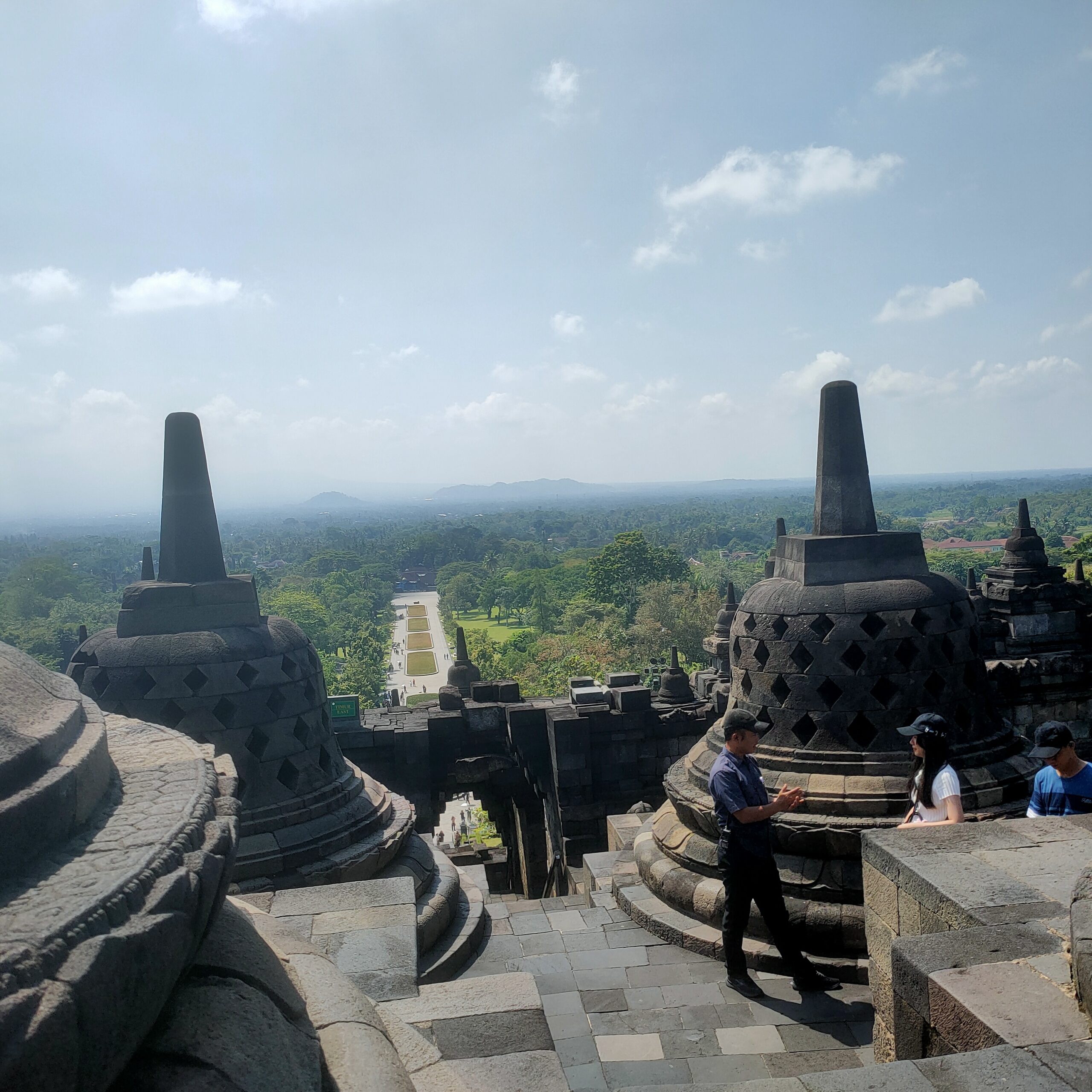 Borobudur temple view from upper terrace looking over green Central Java landscape with perforated stupas and security guard April 2026