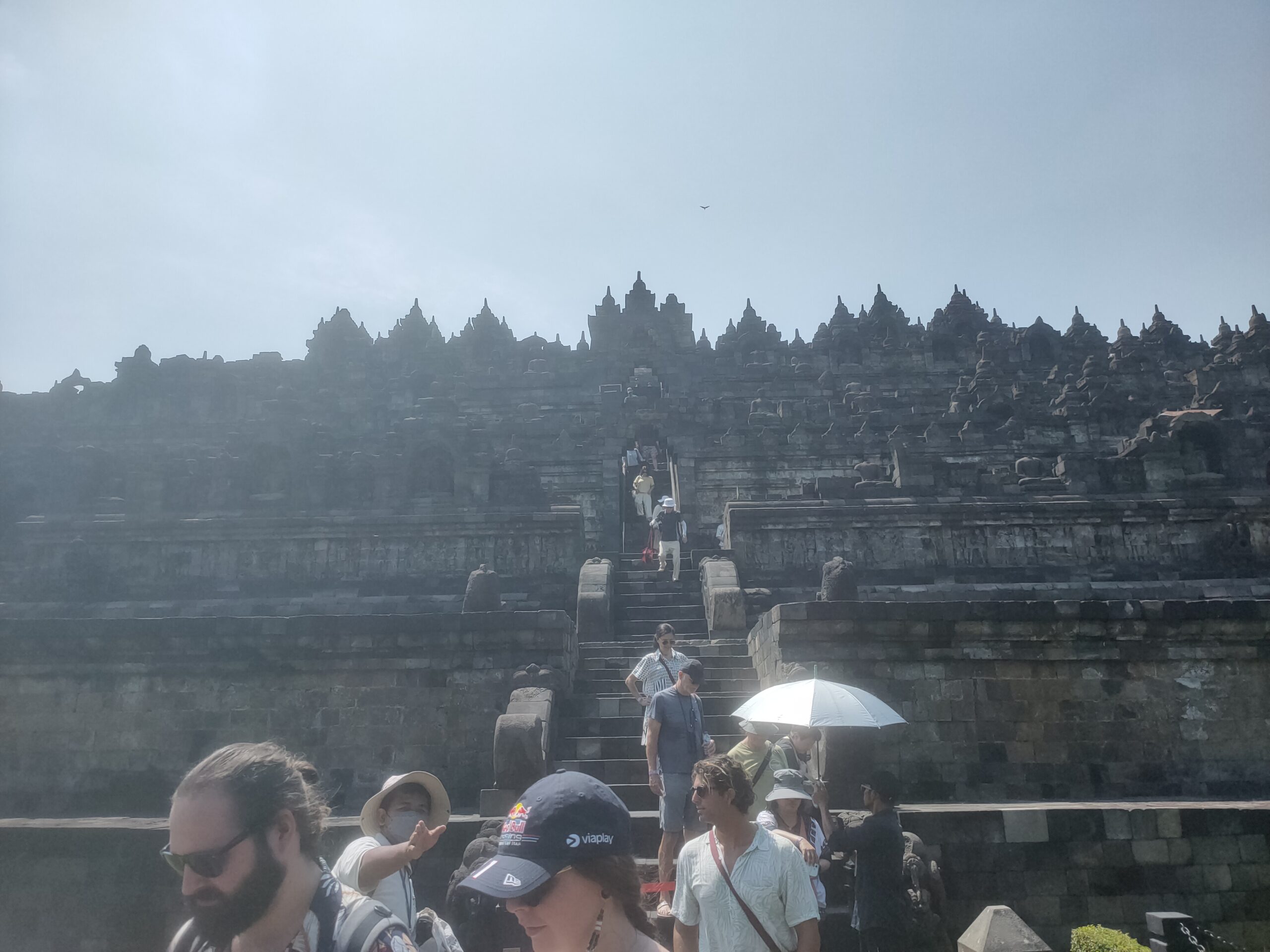 Borobudur temple tourists climbing stairs toward bell shaped stupas on upper terraces Central Java Indonesia April 2026