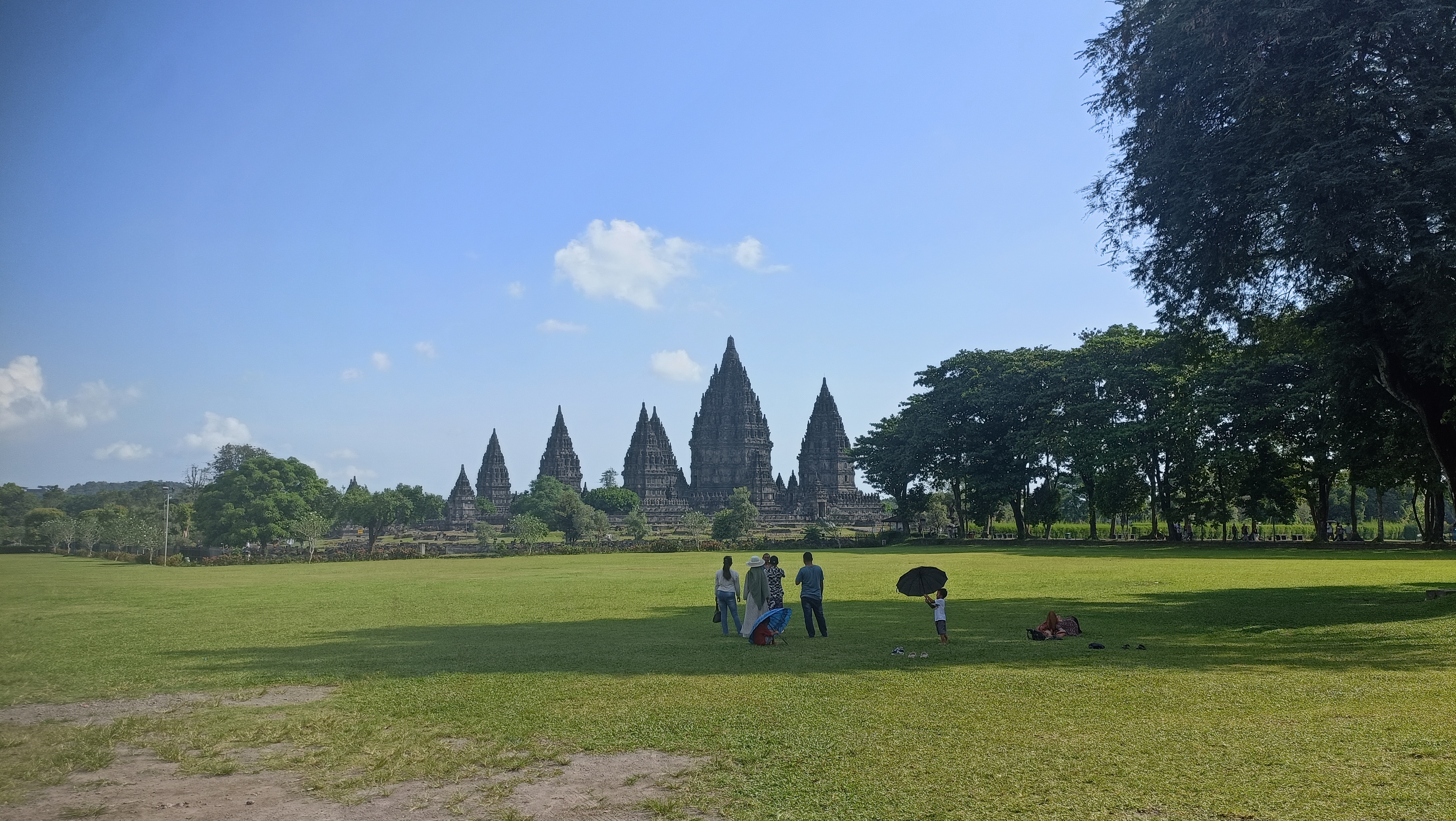 Prambanan Temple: The 00:00 Guide to Java’s Hindu Twin Panoramic view of Prambanan temples with tourists sitting on grass lawn afternoon light Yogyakarta Indonesia
