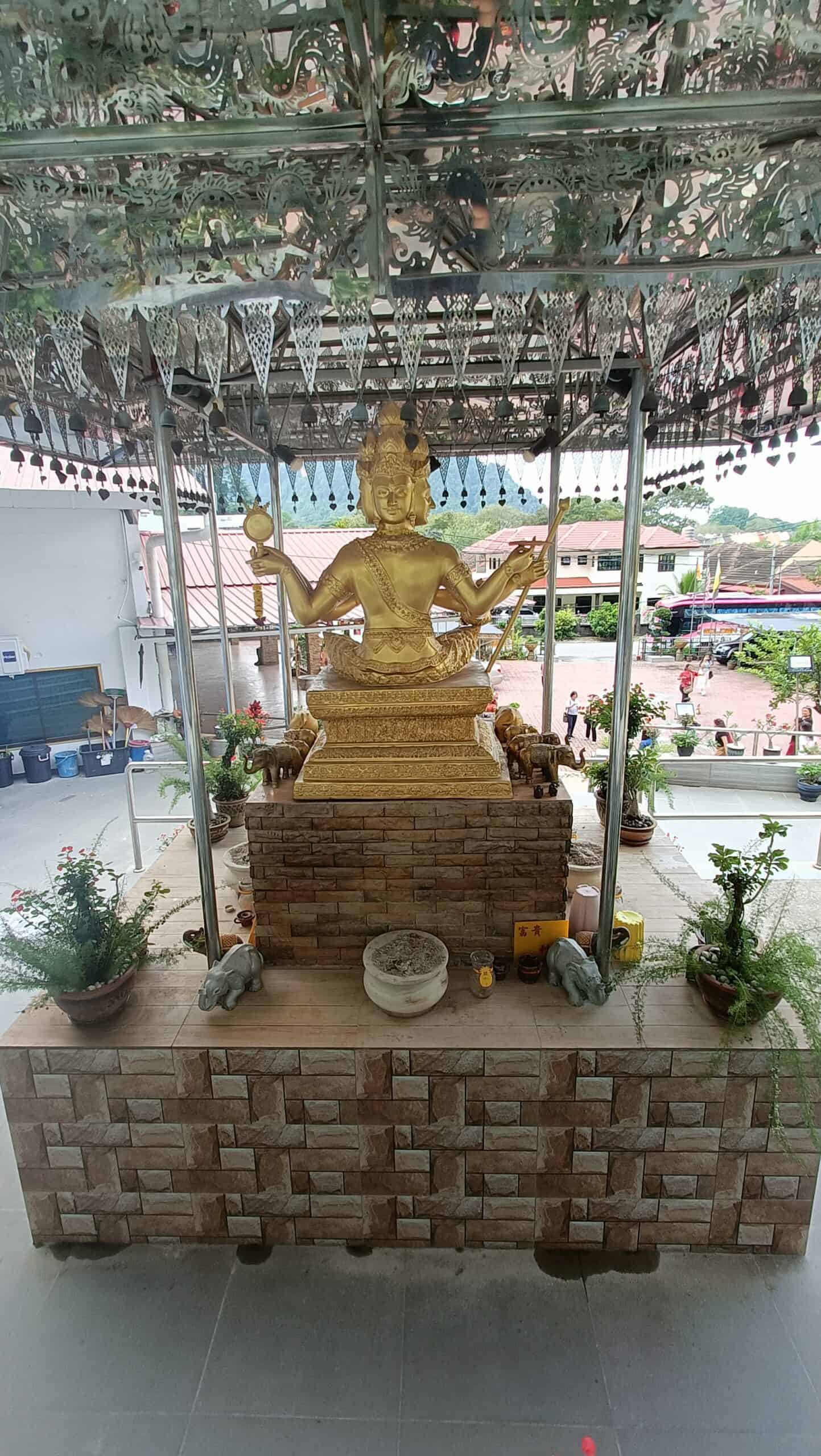 Four-faced Brahma statue under a decorative roof at Wat Puthanimittam Temple Ipoh with offerings at the base`
