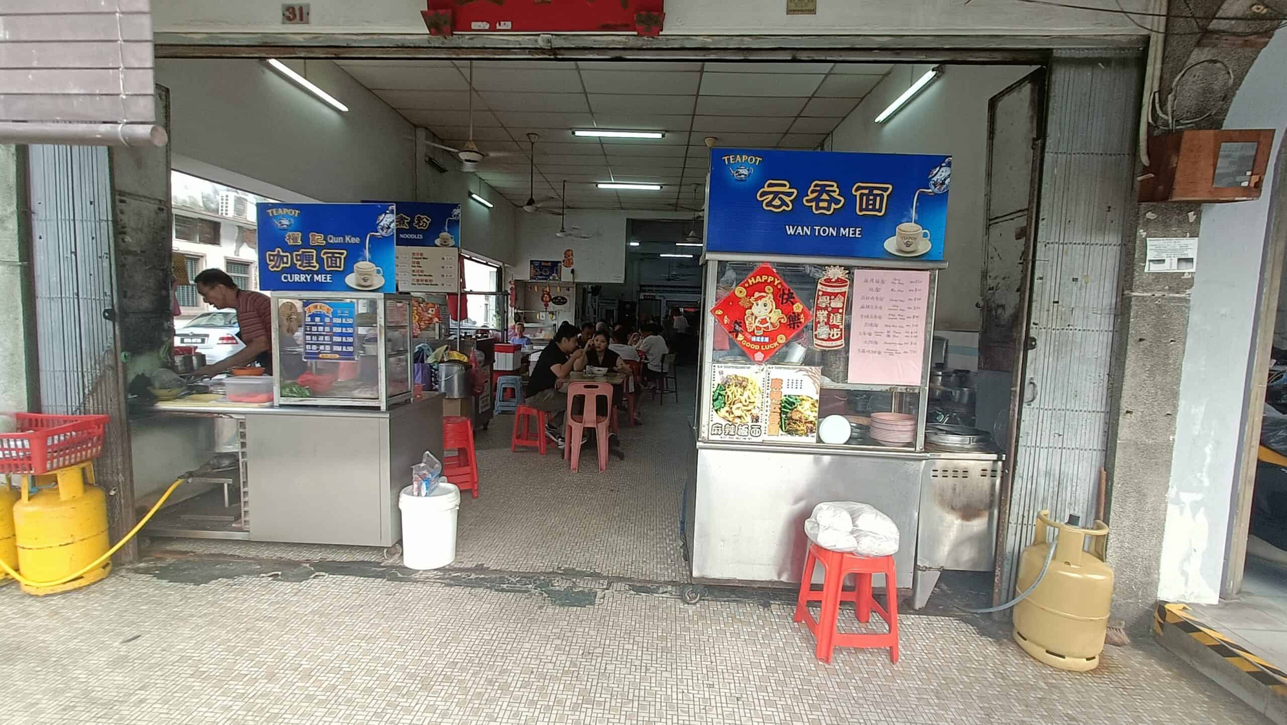 Ah Chow Restaurant storefront in Ipoh with red plastic stools, food posters, and customers dining inside`