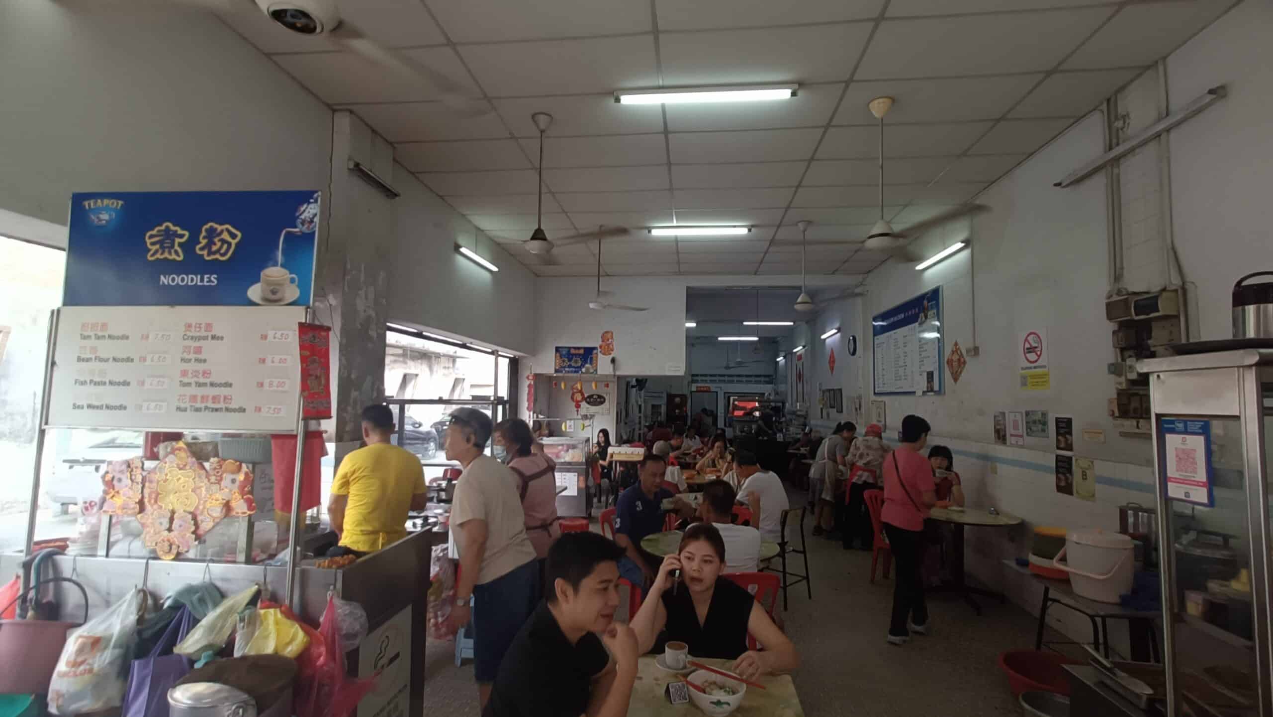 `Interior of Kedai Kopi Ah Chow in Ipoh with red chairs, tables full of customers, and ceiling fans overhead`