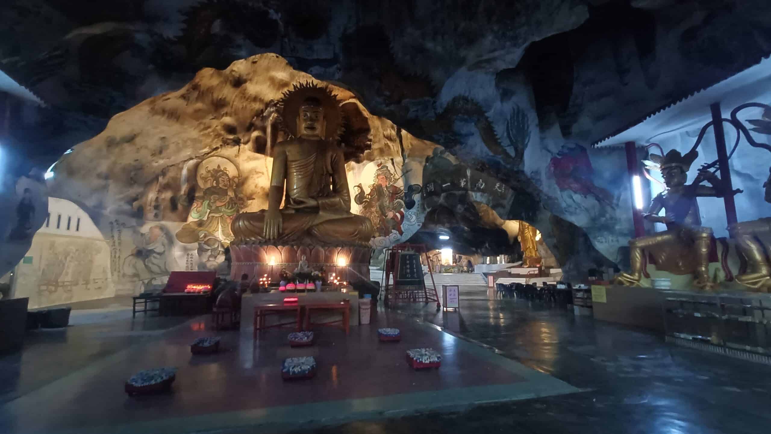 Large seated golden Buddha statue on an altar inside Perak Tong Cave Temple in Ipoh, Perak, with red offering bowls on the shiny floor