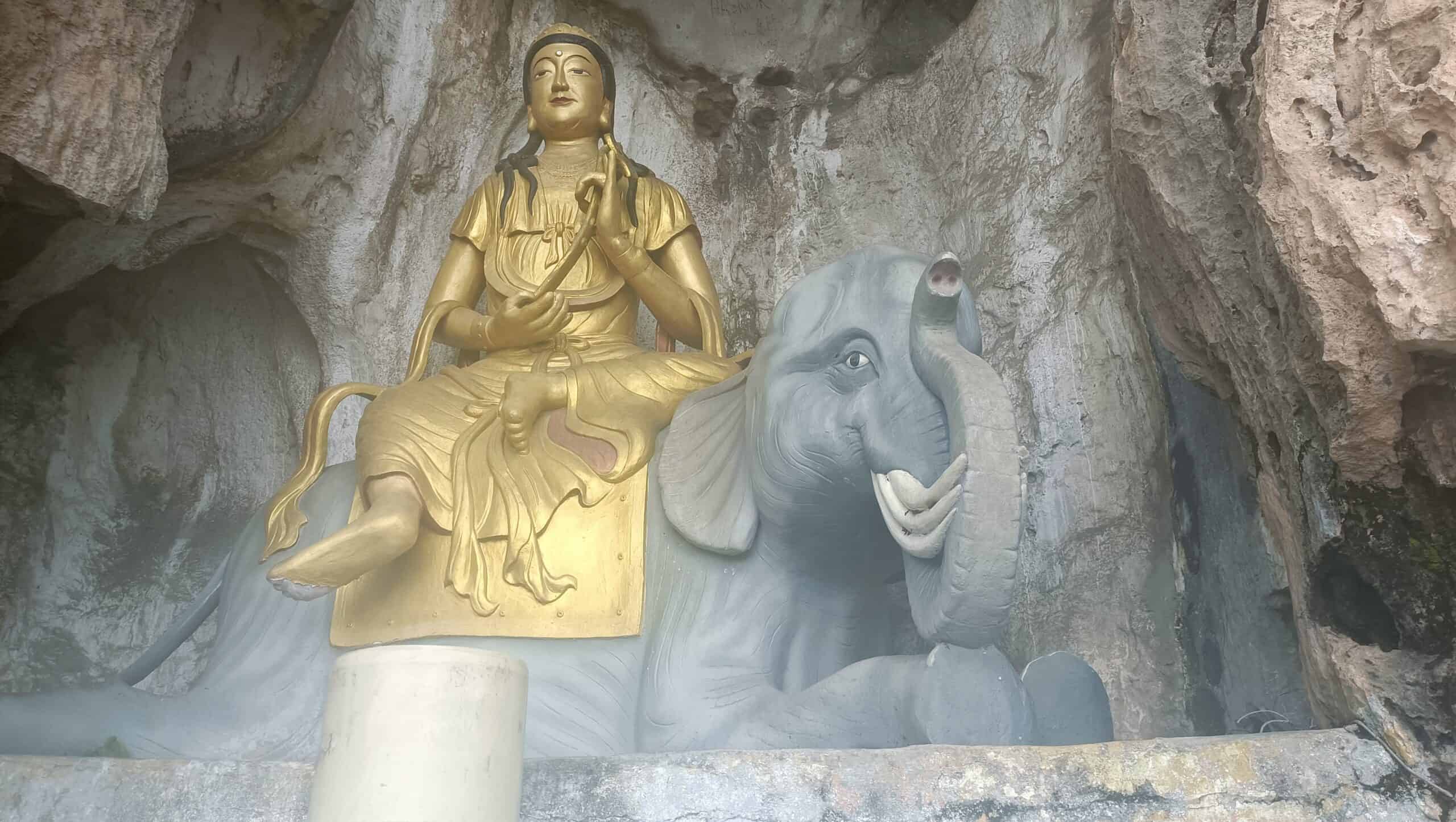 Golden deity statue seated on a grey elephant inside Perak Tong Cave Temple