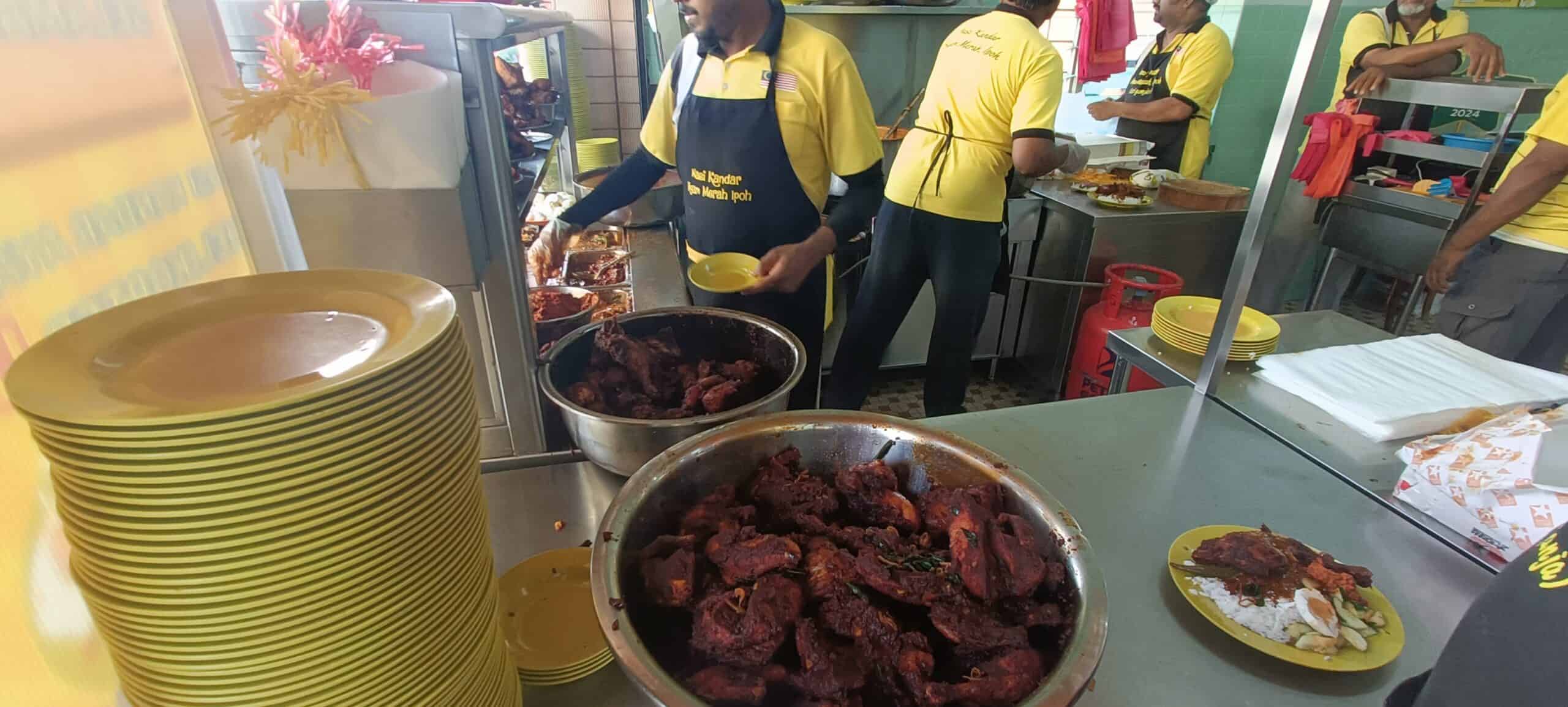 Yellow plates and curry trays at Nasi Ganja Ipoh with staff serving food